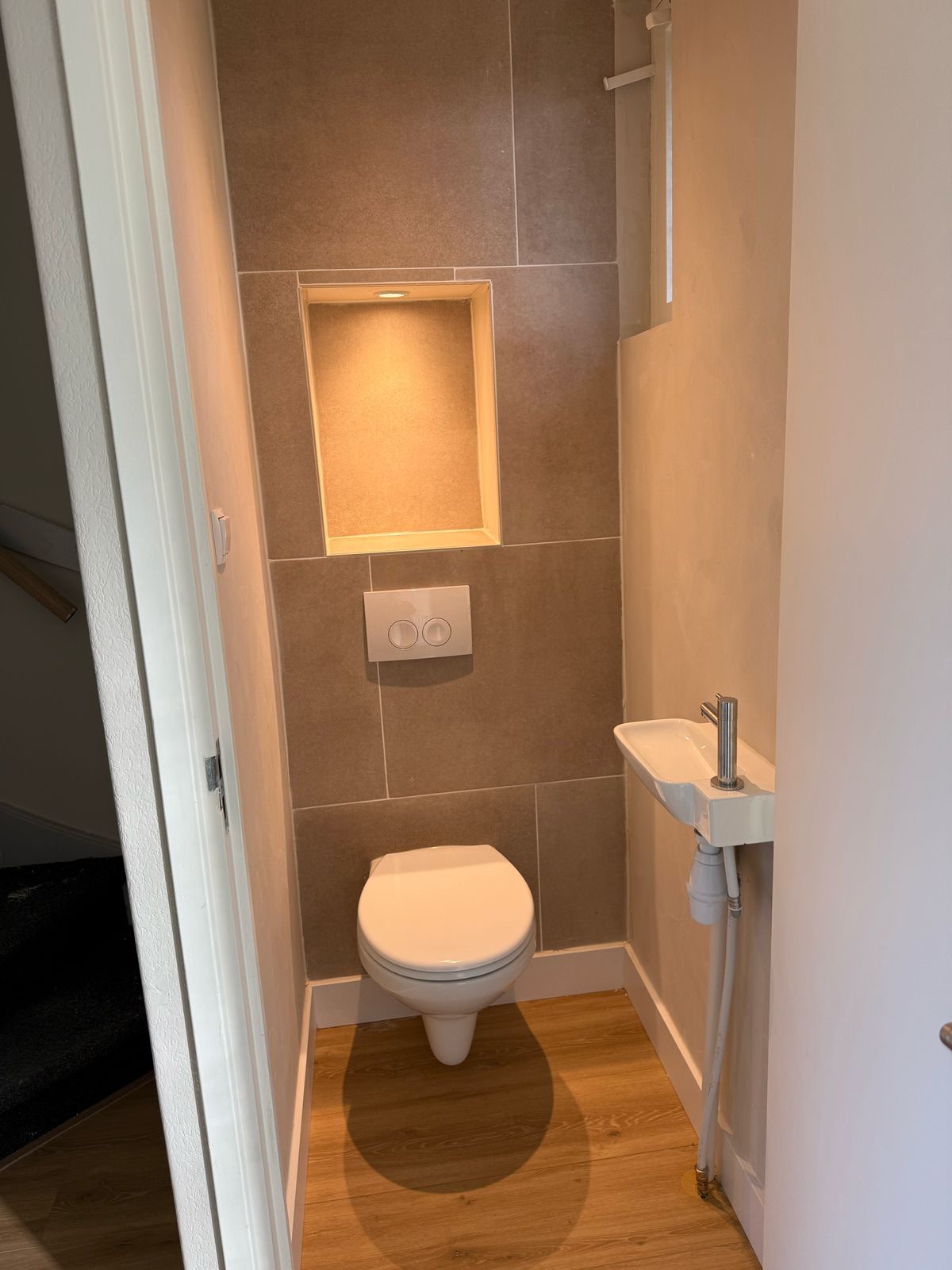 Compact toilet met tegelwand, nisverlichting en wastafel